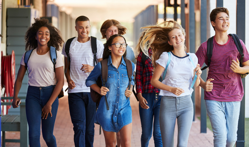 Stock photo of 7 students carrying backpacks and running through a school hallway.