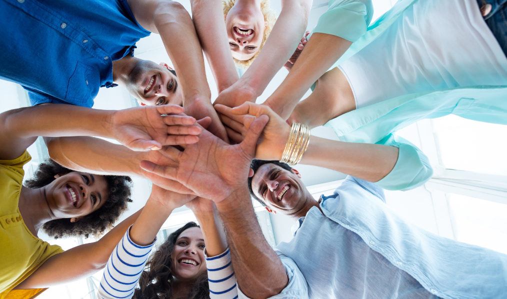A stock photo of people standing in a circle with their hands joined in the center of the circle