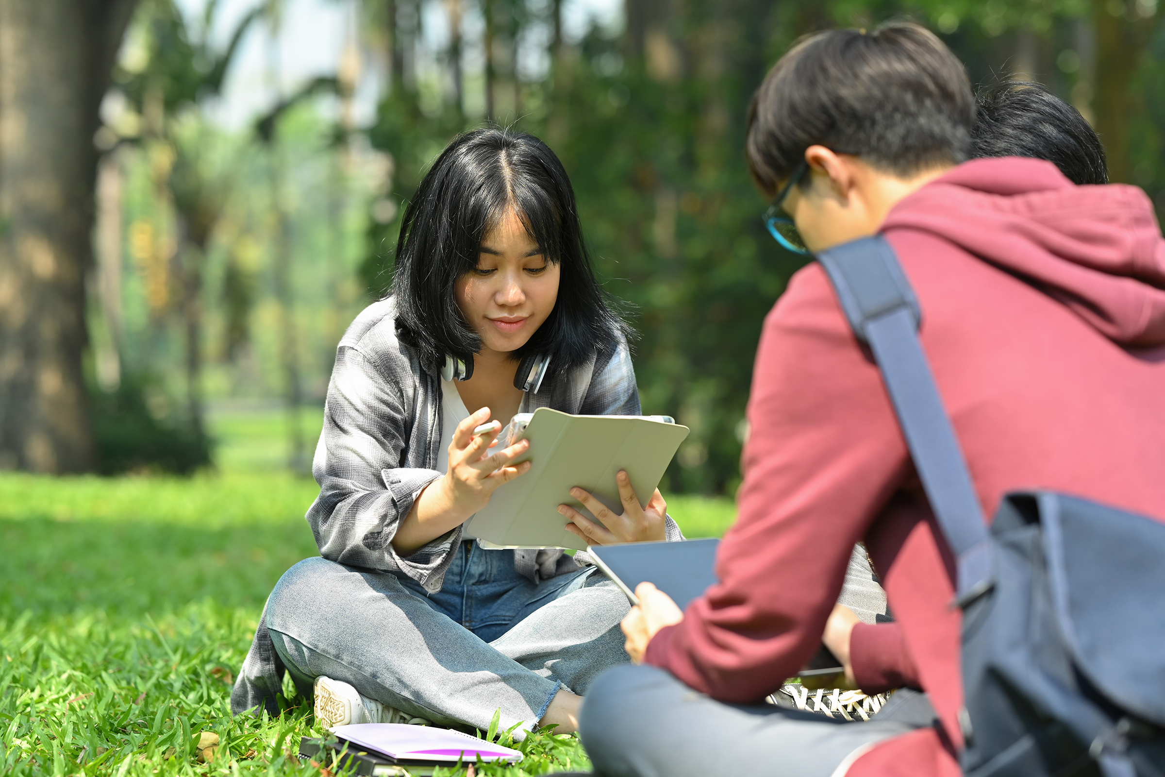 Image of Asian American female student reading books with her friends at summer park. Education and lifestyle concept.