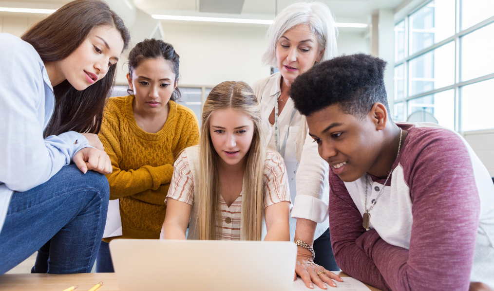 Stock picture of four students and an educator viewing content on a laptop.